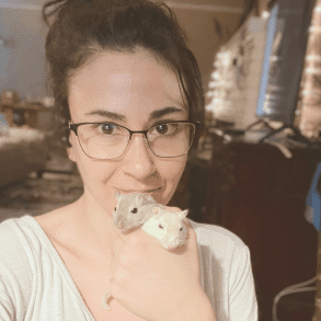 Young woman with glasses holding two gerbils in one hand.